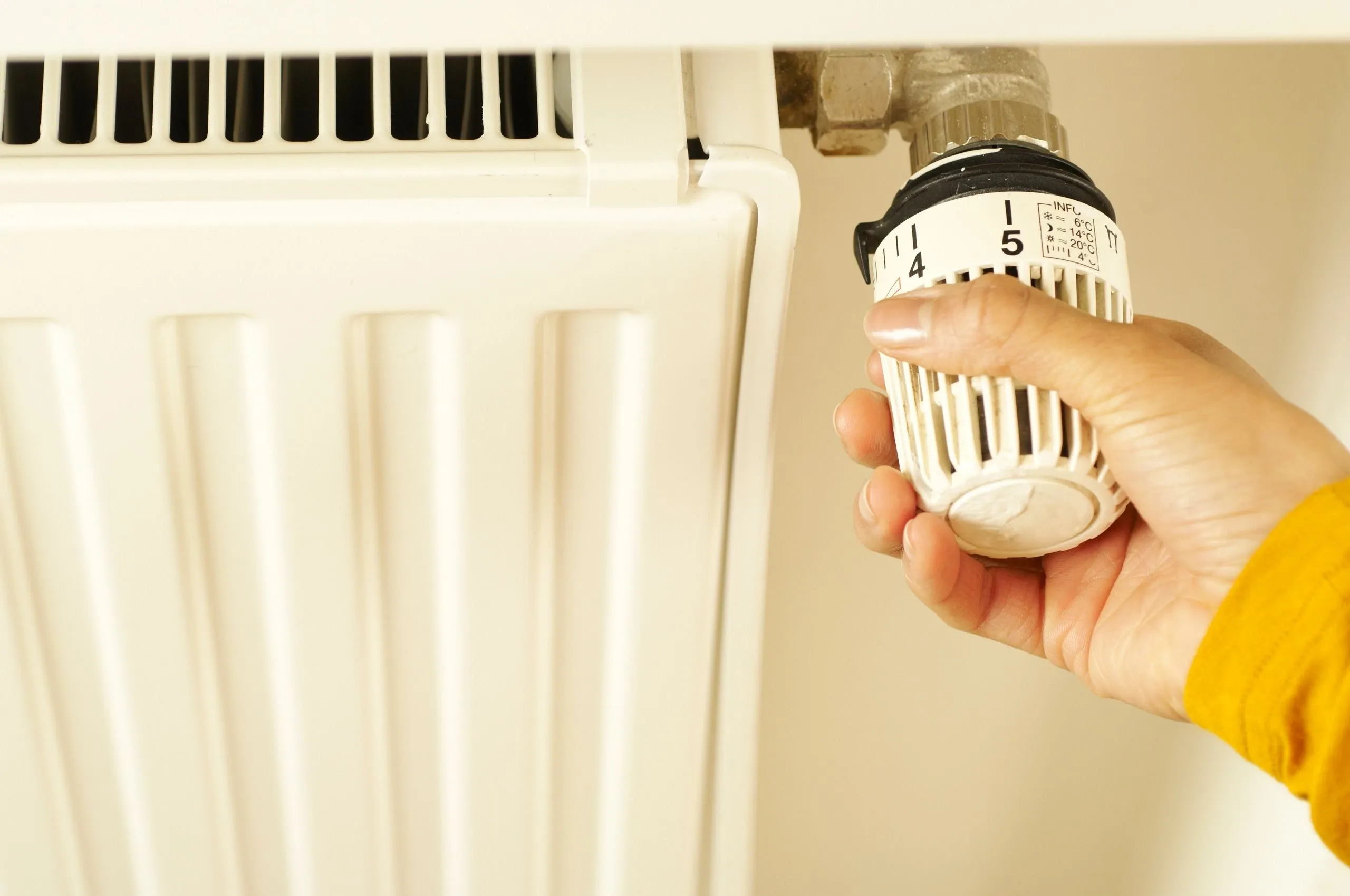 Une main règle le robinet thermostatique d'un radiateur blanc