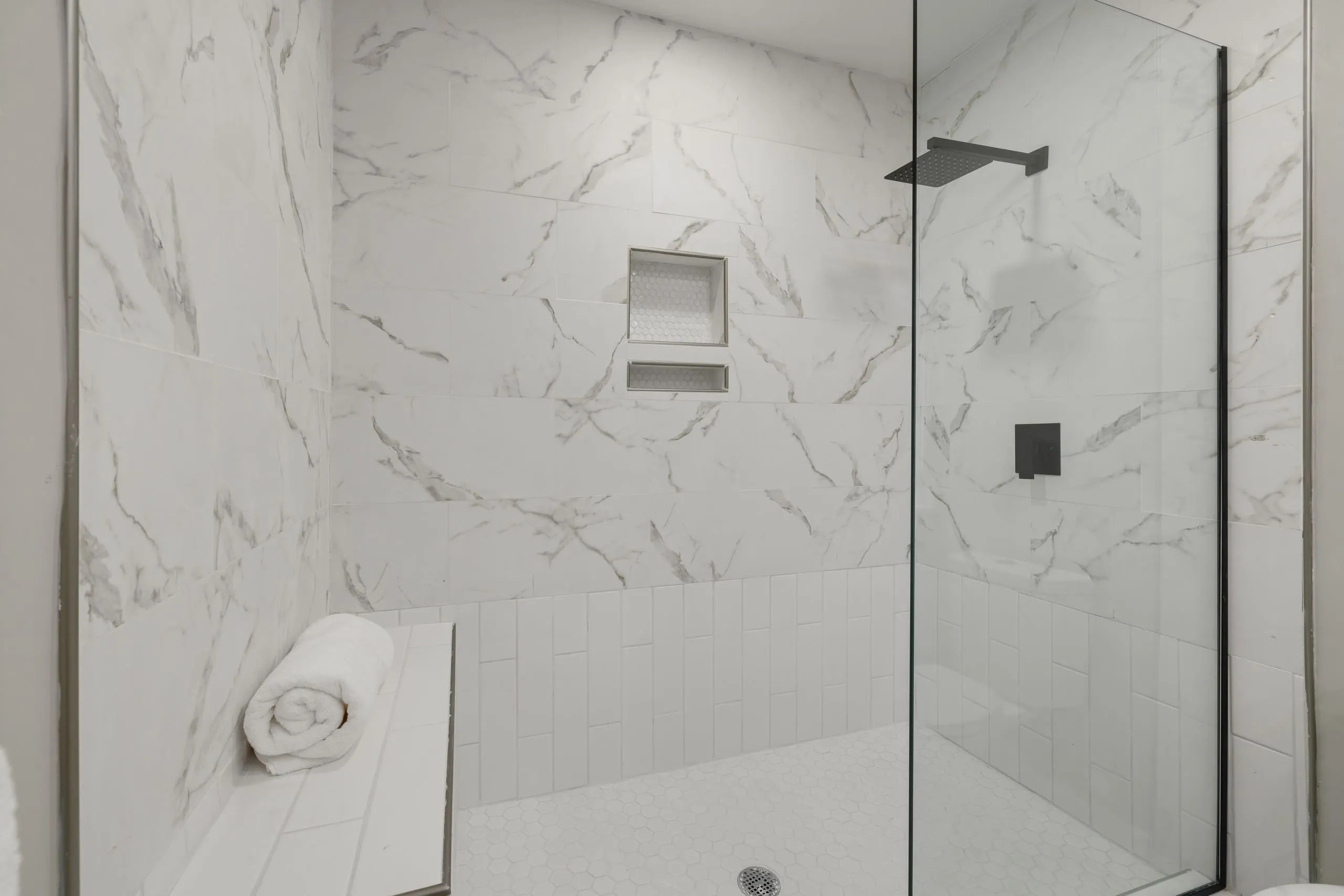 Une grande douche vitrée en carrelage effet marbre, avec niche et banc