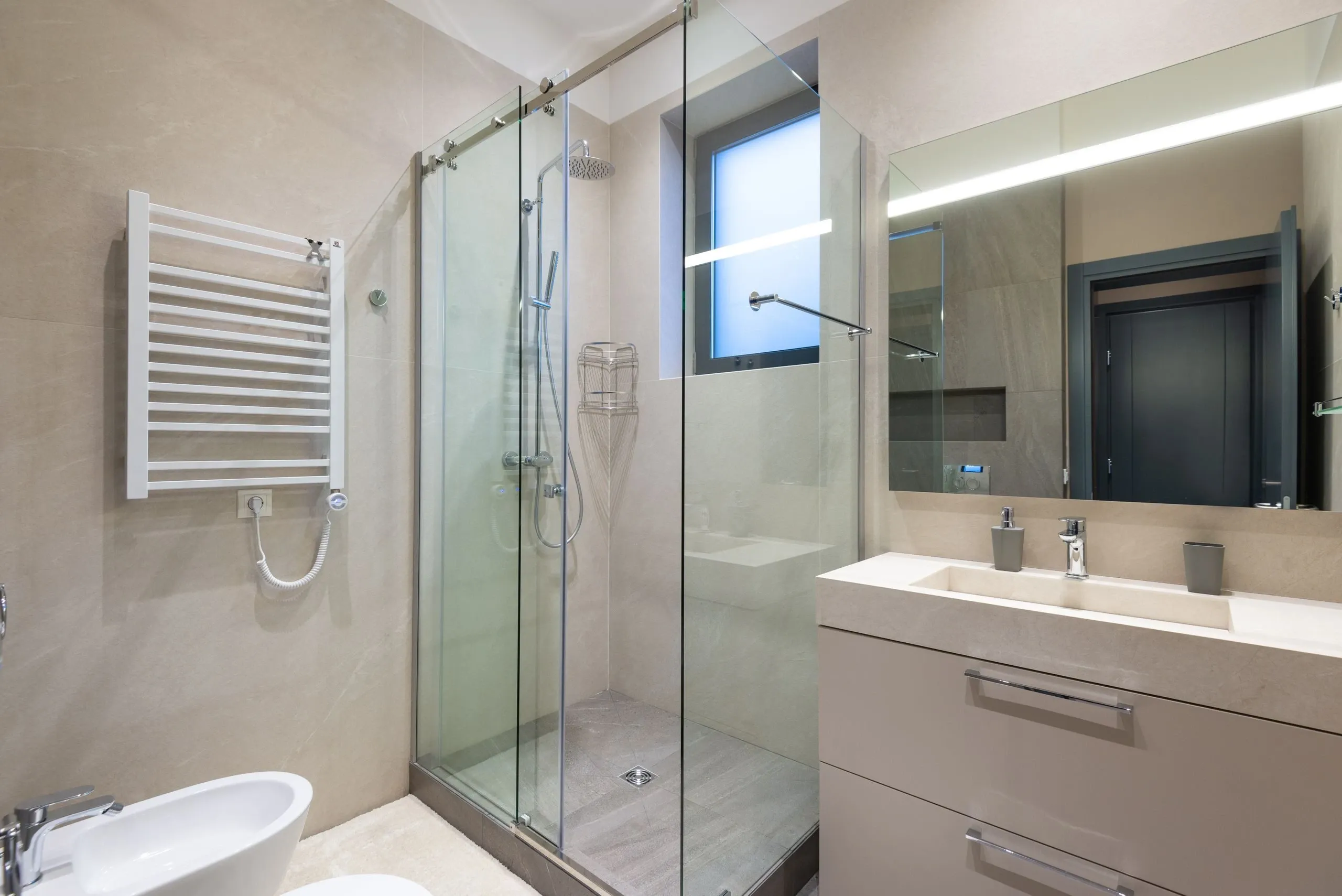 Une salle de bains claire : douche vitrée, meuble vasque et sèche-serviettes