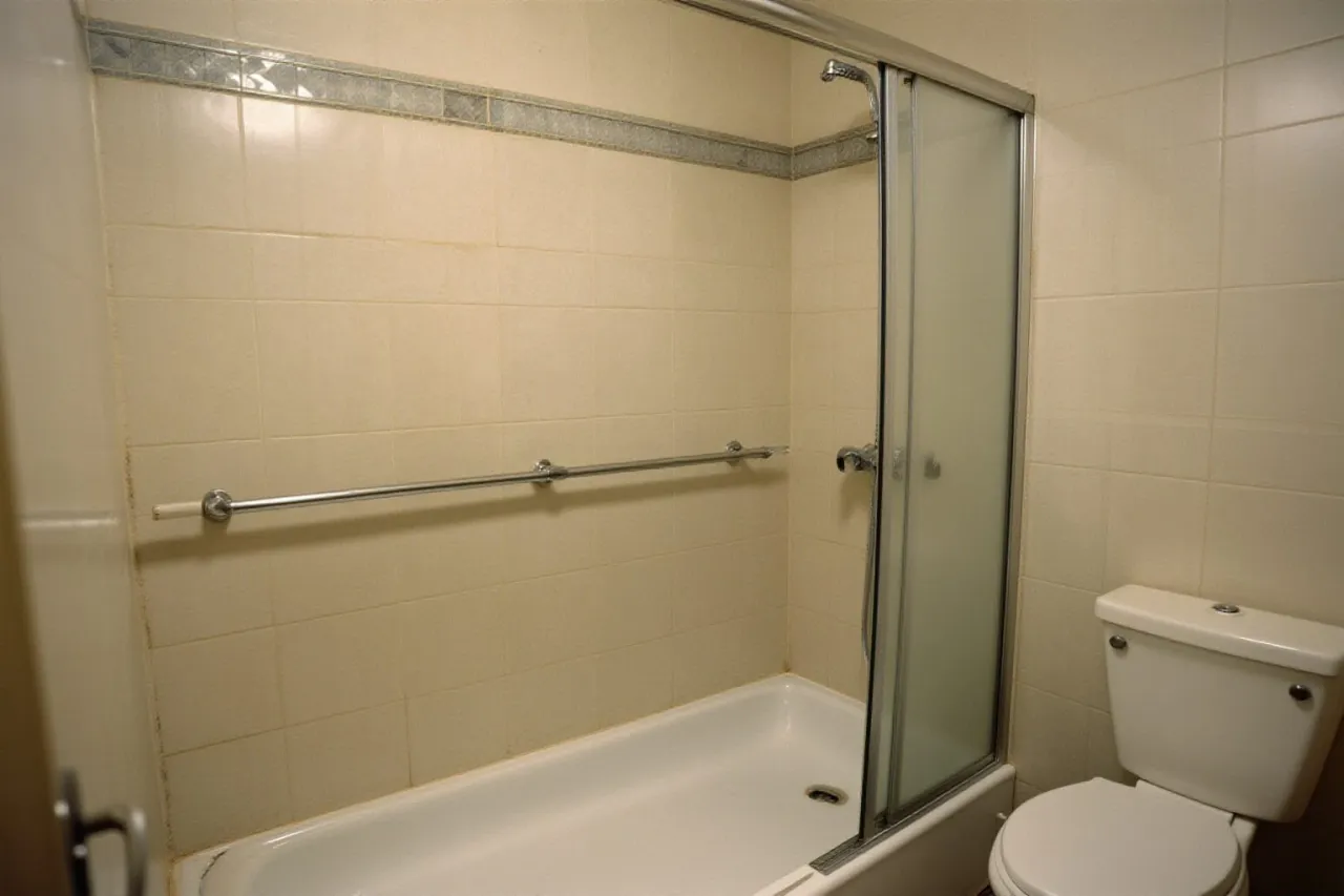 La même pièce avant travaux : baignoire, porte de douche coulissante, carrelage beige
